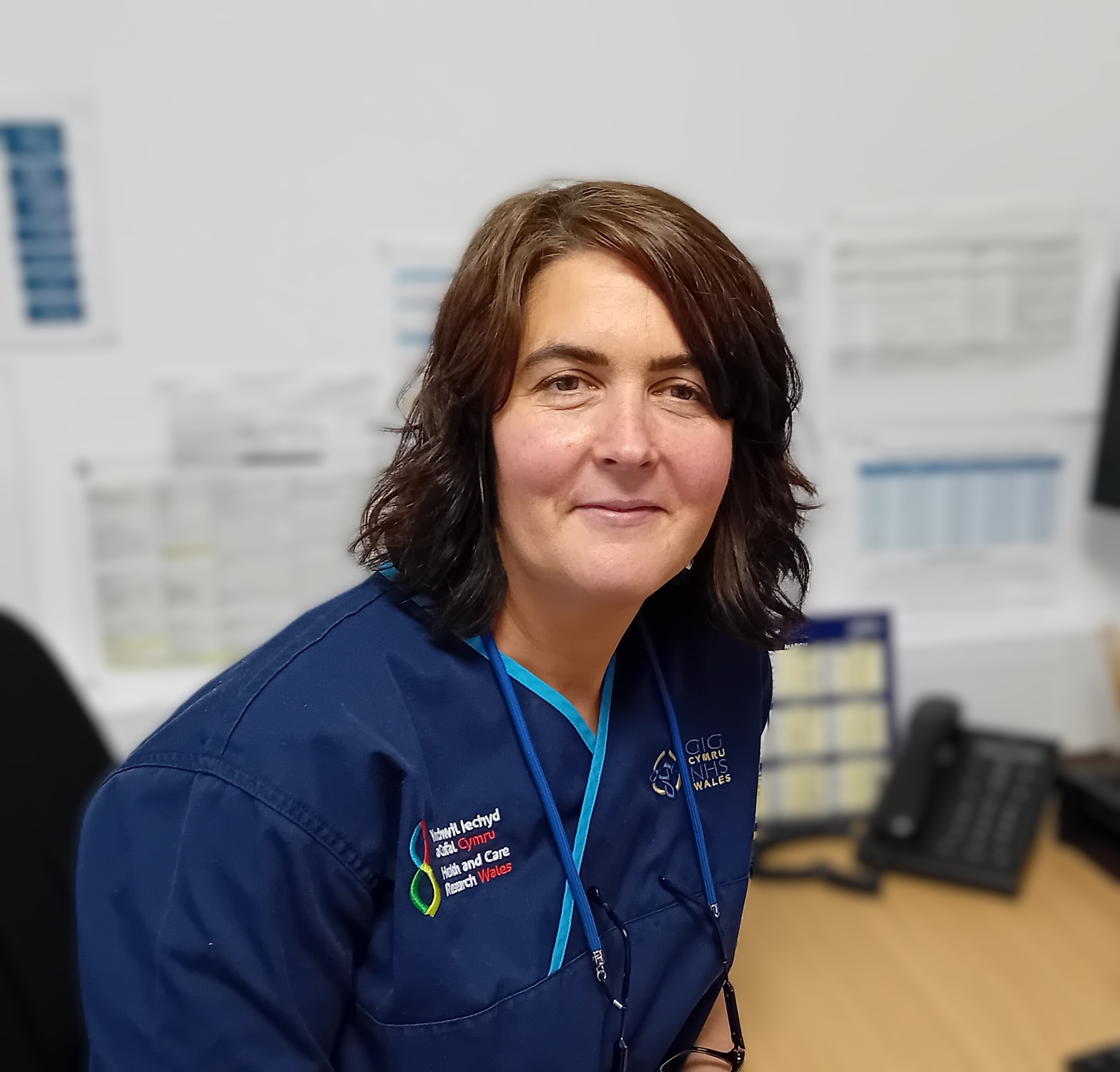 Cardiff Cancer Research Hub lead research nurse Kate Gilmour sitting at desk in blue uniform